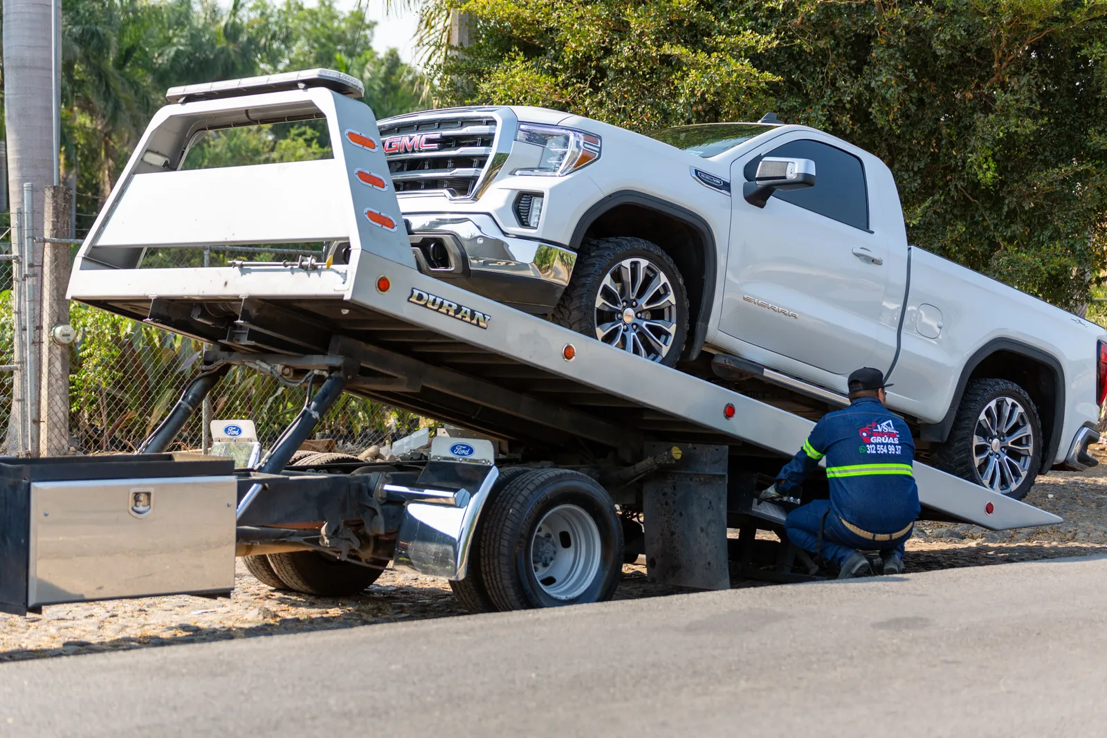 Tow truck operator loading white GMC pickup truck on street in daytime. Tow truck driver hours of service: the time record to keep