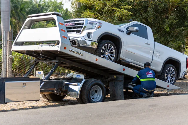 Tow truck operator loading white GMC pickup truck on street in daytime. Tow truck driver hours of service: the time record to keep