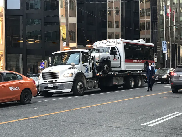 Wheel-Trans vehicle W112 (112) being lifted by a Freightliner tow truck, AK 12807. Towing company equipment: a reviewer's notes