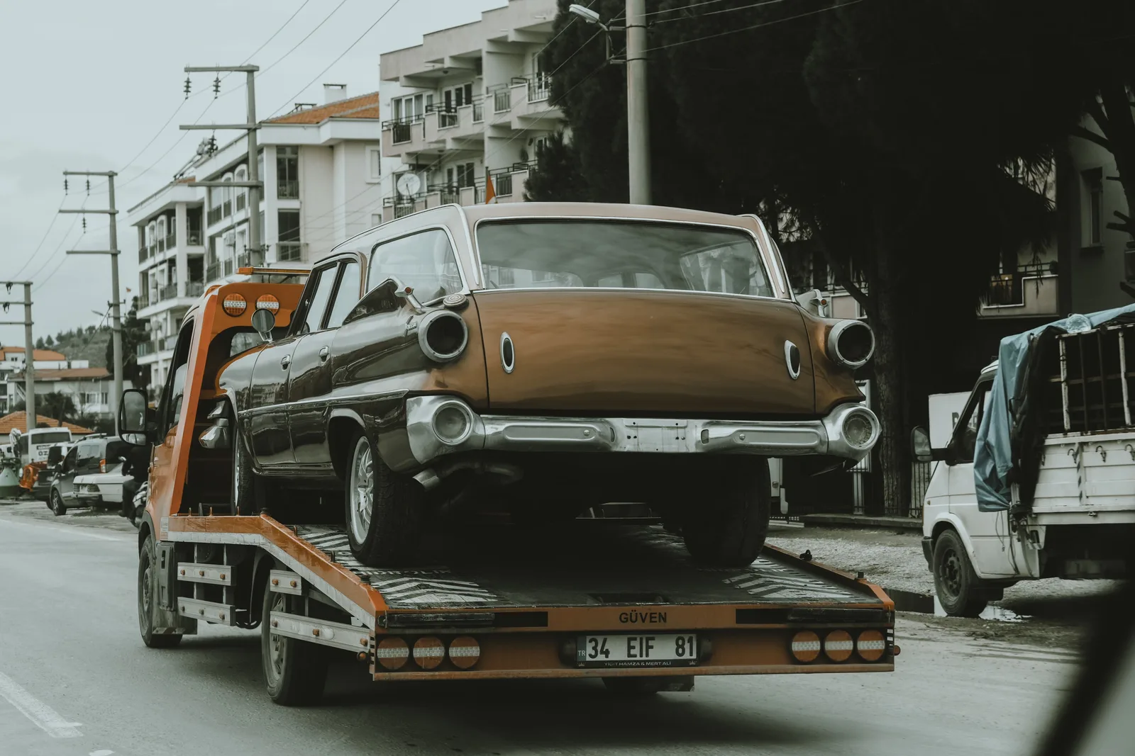 A vintage car loaded on a tow truck in a city street, surrounded by modern buildings. Daily operating checklist for a towing company for new owners