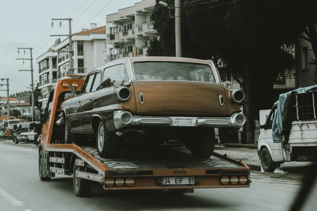 A vintage car loaded on a tow truck in a city street, surrounded by modern buildings. Daily operating checklist for a towing company for new owners